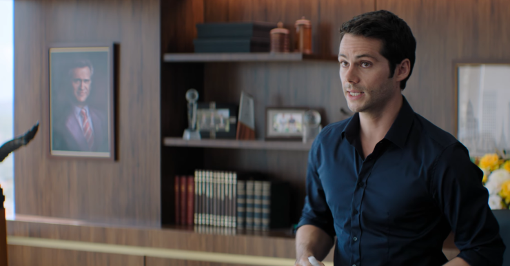 Dylan O’Brien as Bradley Preston in his office in 'Send Help'; a framed Bruce Campbell portrait is visible on the bookshelf behind him
