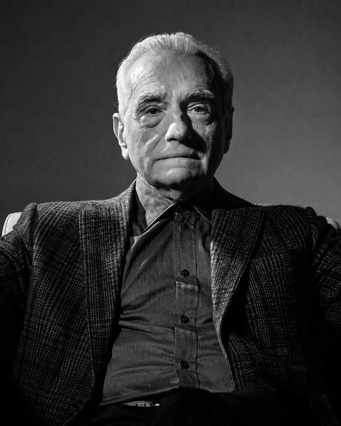 A black-and-white portrait of Martin Scorsese, seated and looking at the camera